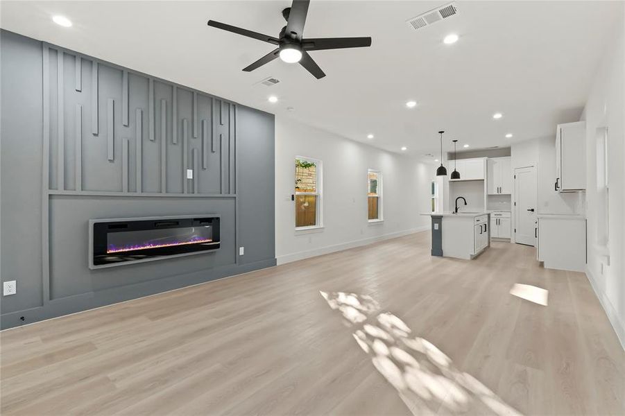 Unfurnished living room featuring light wood-style flooring, ceiling fan, recessed lighting, and a glass covered fireplace