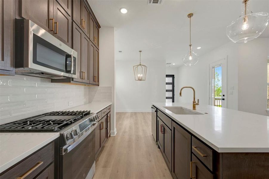 Kitchen featuring dark wood cabinetry, white countertops, a gas range with an over-the-range microwave, and a white subway tile backsplash