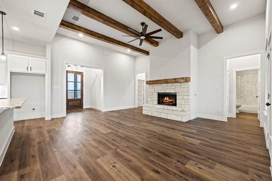 Unfurnished living room with a stone fireplace, dark wood finished floors, and visible vents