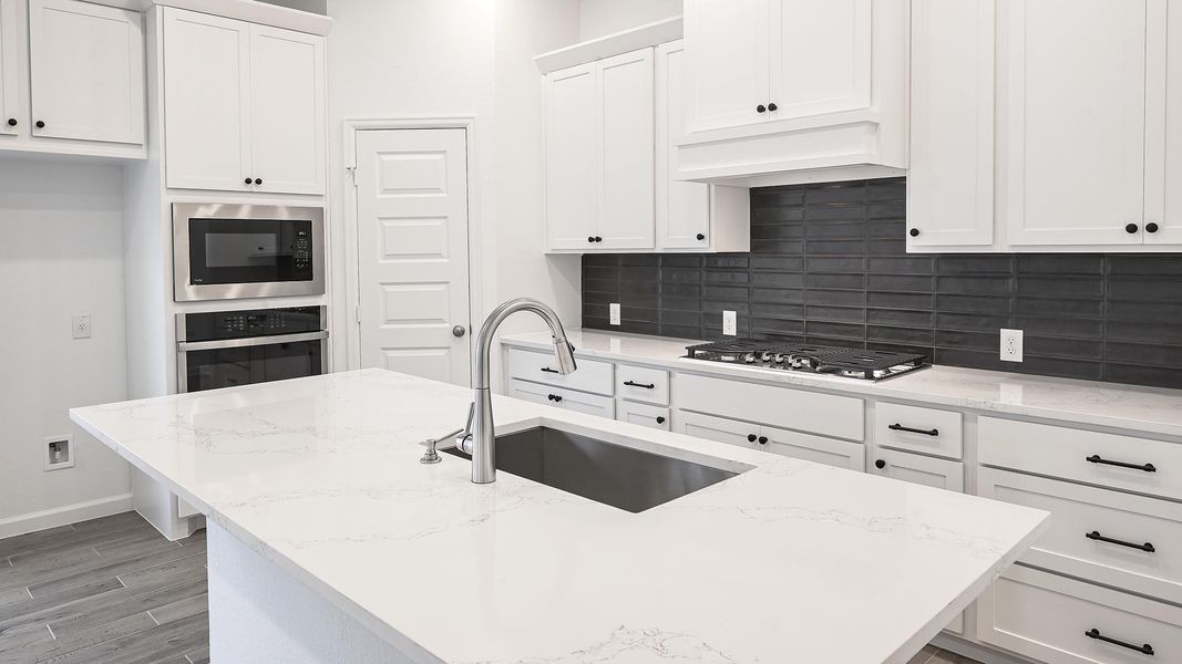 Kitchen featuring white cabinets, a kitchen island with sink, light stone counters, stainless steel appliances, and backsplash Kitchen featuring white cabinets, a kitchen island with sink, light stone counters, stainless steel appliances, and backsplash