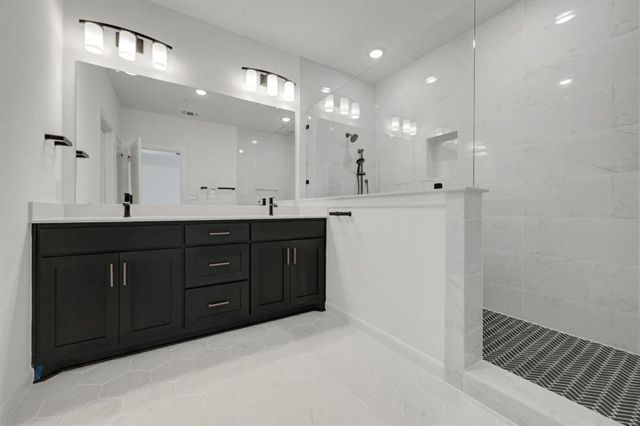 Contemporary bathroom featuring a dark wood double vanity with white countertops, expansive wall-mounted mirror, and a spacious walk-in shower with white tile walls and a patterned floor Contemporary bathroom featuring a dark wood double vanity with white countertops, expansive wall-mounted mirror, and a spacious walk-in shower with white tile walls and a patterned floor
