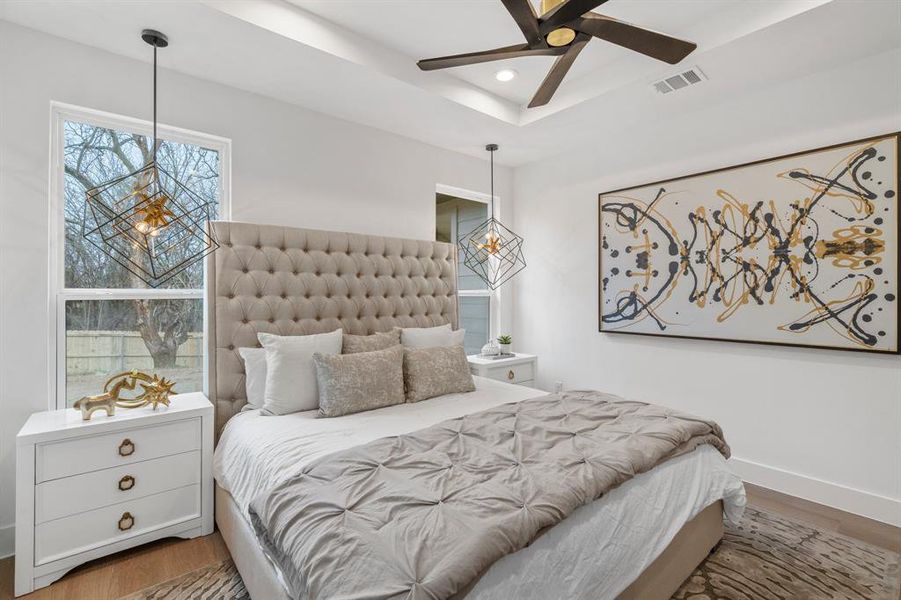 Bedroom with ceiling fan, a tray ceiling, and hardwood / wood-style flooring