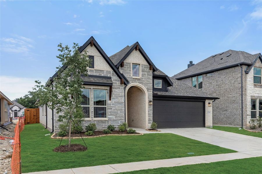 Two-story stone and brick home with arched entry, two-car garage, and manicured front lawn