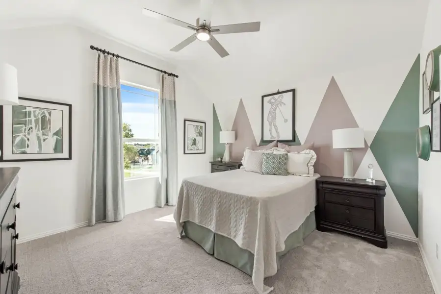 Bedroom with geometric accent wall, ceiling fan, carpet flooring, and large window with natural light