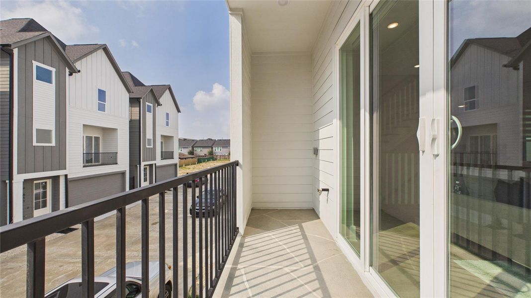 This photo shows a modern balcony with sleek railing overlooking a row of contemporary townhouses. The area is bright, with sliding glass doors providing access from indoors, ideal for enjoying fresh air and views of the neighborhood.