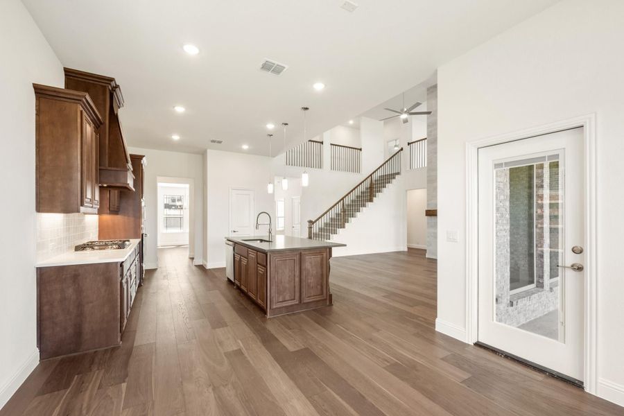 Open kitchen with dark wood cabinets, center island, and hardwood floors leading to a two-story staircase Open kitchen with dark wood cabinets, center island, and hardwood floors leading to a two-story staircase