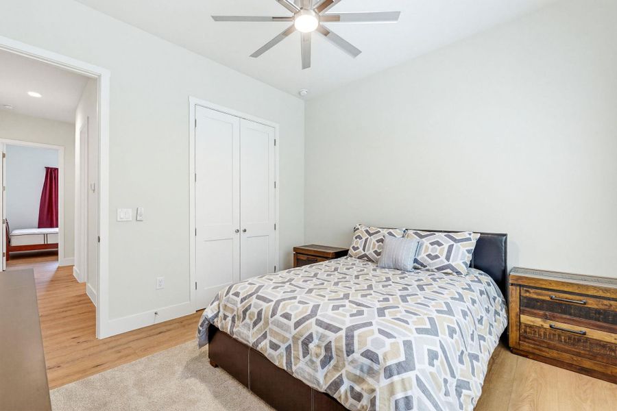 A quiet secondary bedroom features warm wood flooring and a modern ceiling fan for ultimate comfort.