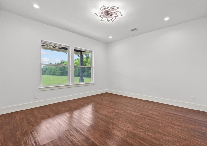 Elegant primary suite featuring rich wood like flooring, designer lighting, oversized windows with peaceful property views, and a sophisticated contemporary design.