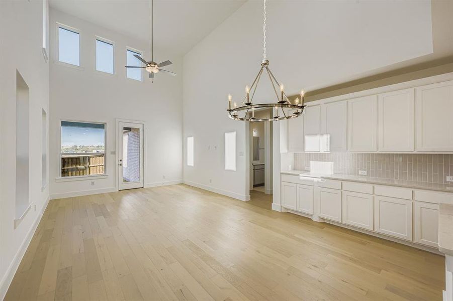 Unfurnished dining area with light wood finished floors, a towering ceiling, ceiling fan, a chandelier, and plenty of natural light