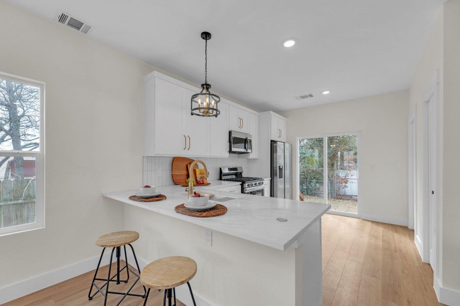 Kitchen featuring a peninsula, light wood finished floors, white cabinets, a breakfast bar, and stainless-steel Samsung appliance package.