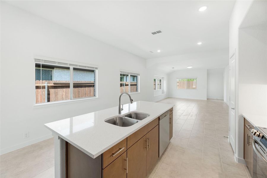 Kitchen island with double sink, white quartz countertop, and wood cabinets opening to living area