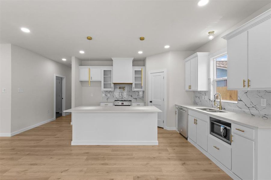 Open-concept kitchen featuring a central island, white cabinetry with gold-tone hardware, and light wood-finish flooring