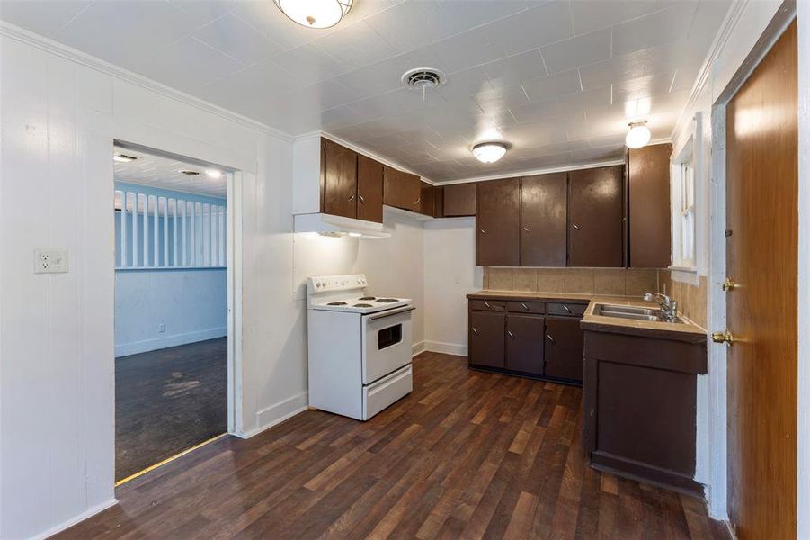 Kitchen featuring dark brown cabinets, electric stove, light countertops, under cabinet range hood, and ornamental molding Kitchen featuring dark brown cabinets, electric stove, light countertops, under cabinet range hood, and ornamental molding