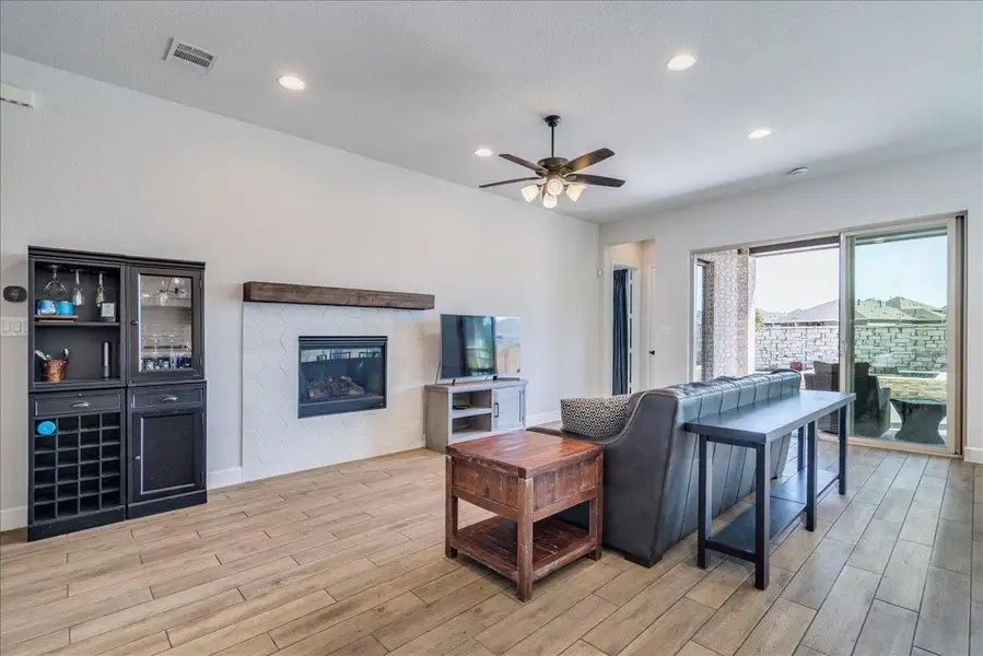 Living area with wood finish floors, recessed lighting, a glass covered fireplace, and a ceiling fan