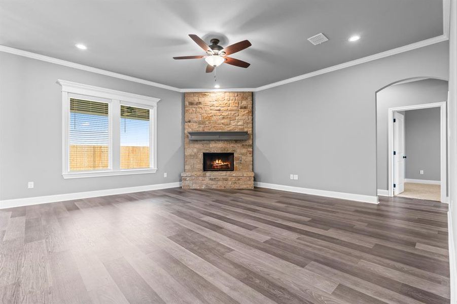 Living room with a stone fireplace, dark wood finished floors, visible vents, ceiling fan, and arched walkways Living room with a stone fireplace, dark wood finished floors, visible vents, ceiling fan, and arched walkways