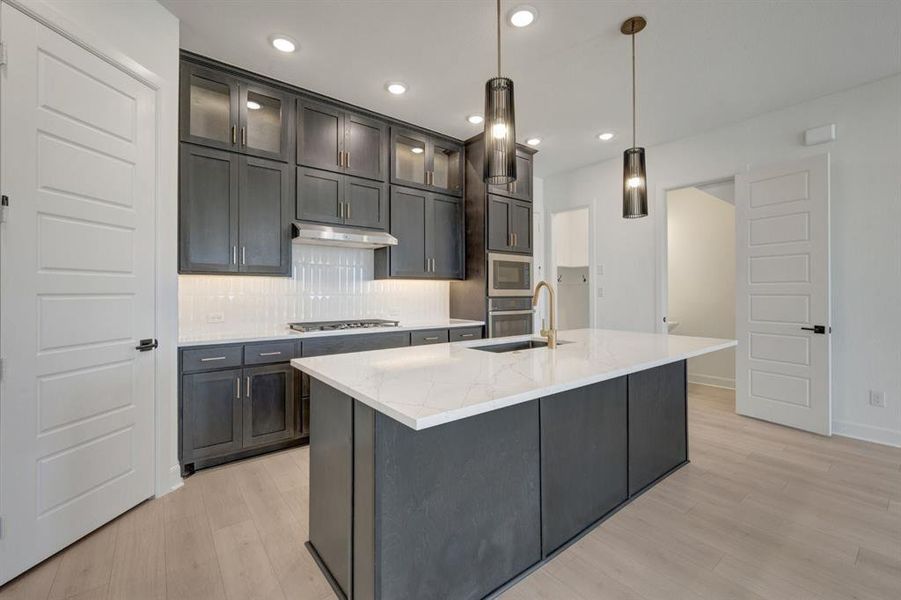 Modern kitchen featuring dark cabinetry, white quartz countertops, stainless steel appliances, and light wood-finish flooring Modern kitchen featuring dark cabinetry, white quartz countertops, stainless steel appliances, and light wood-finish flooring