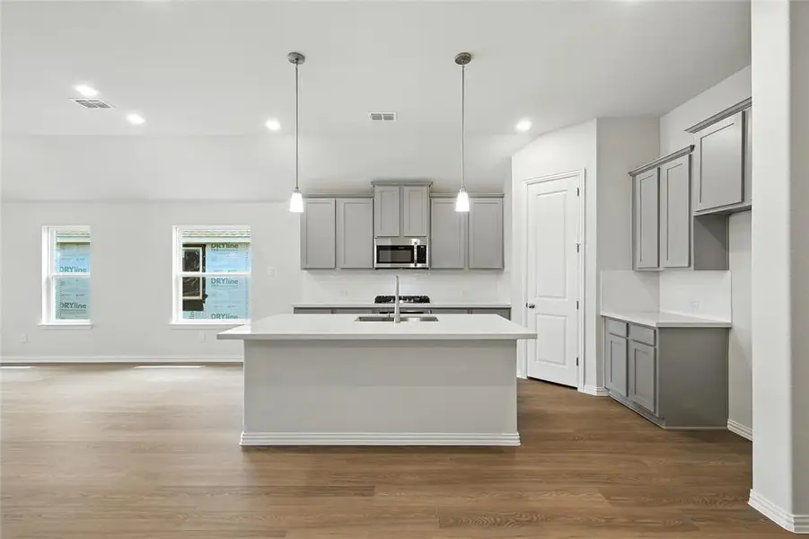Kitchen with gray cabinetry, a center island with sink, dark wood-style floors, decorative backsplash, and stainless steel microwave