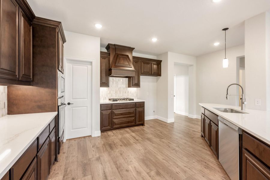 Kitchen with dark wood cabinets, white quartz countertops, custom range hood, and light hardwood floors