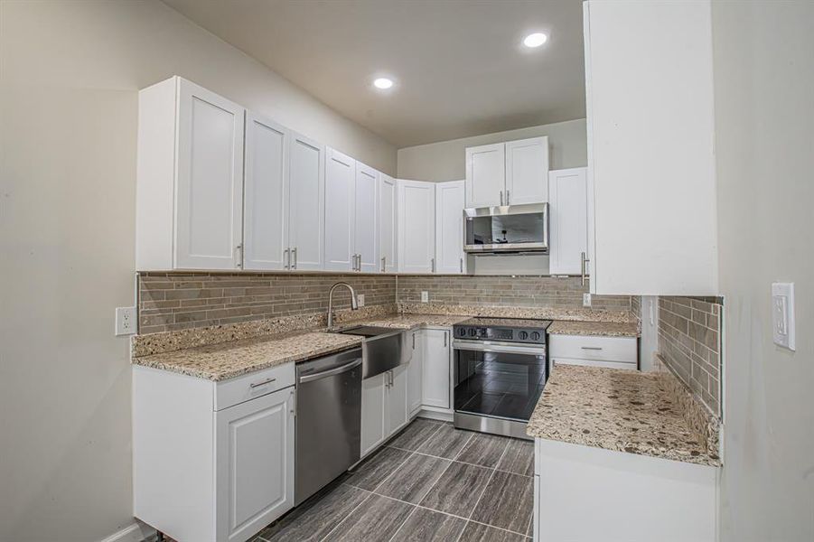 Kitchen featuring white cabinetry, backsplash, appliances with stainless steel finishes, and a sink