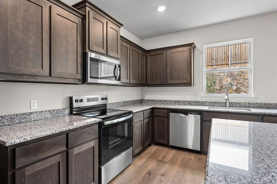 Kitchen with dark brown cabinets, appliances with stainless steel finishes, light stone countertops, light wood-style floors, and recessed lighting Kitchen with dark brown cabinets, appliances with stainless steel finishes, light stone countertops, light wood-style floors, and recessed lighting