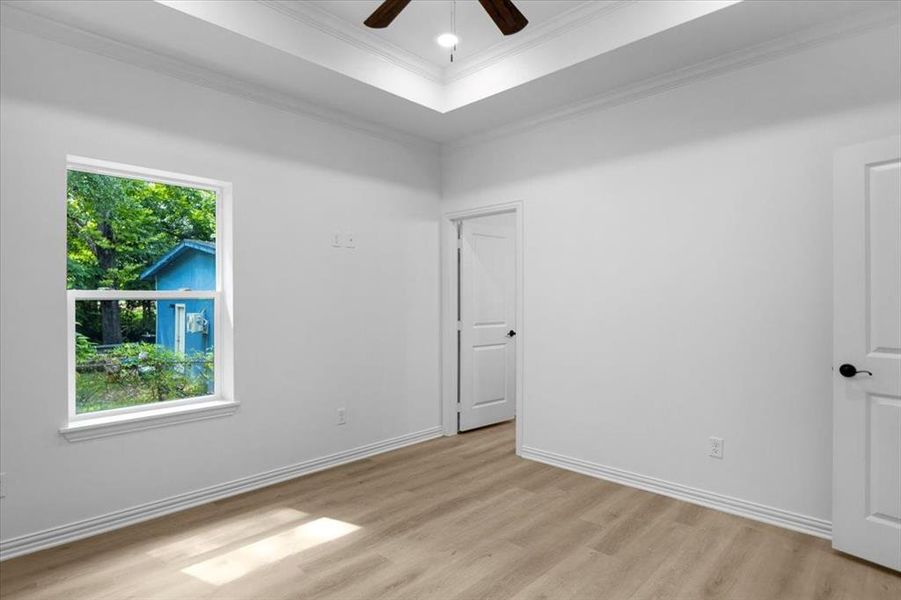 Unfurnished bedroom with a tray ceiling, a ceiling fan, light wood-style flooring, and crown molding
