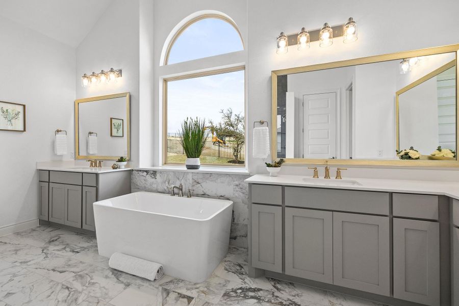 Full bathroom featuring marble look tile flooring, two vanities, a freestanding bath, and vaulted ceiling