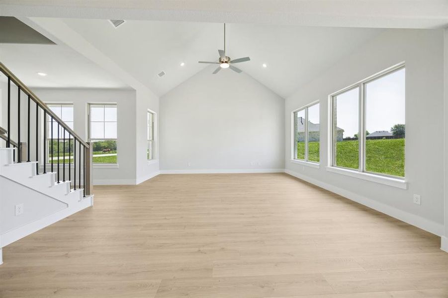 Unfurnished living room with light wood finished floors, healthy amount of natural light, stairway, recessed lighting, and high vaulted ceiling