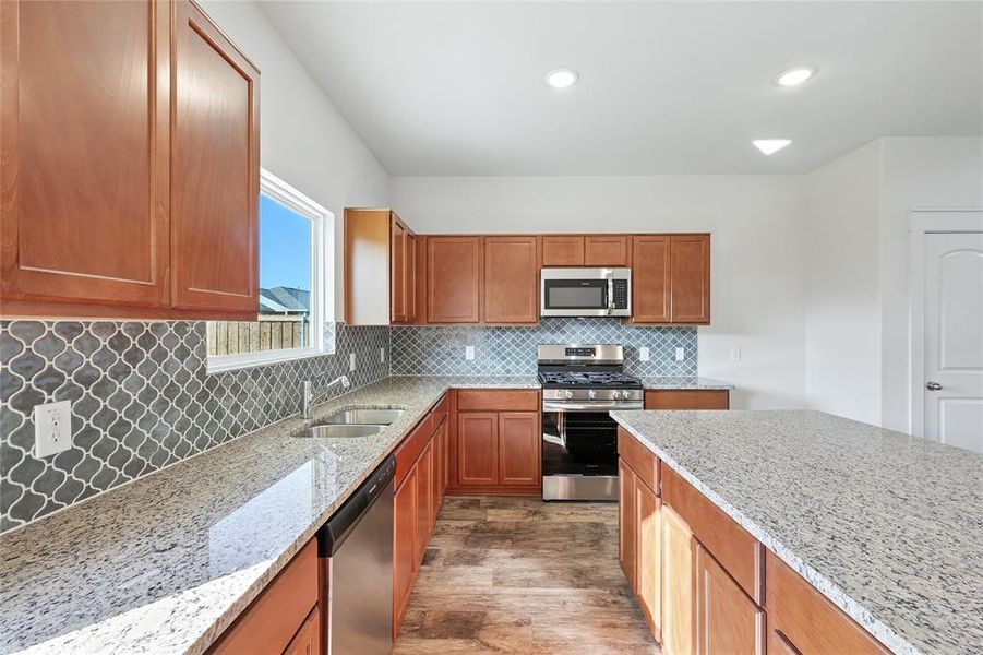 Kitchen featuring brown cabinets, appliances with stainless steel finishes, backsplash, light stone counters, and recessed lighting Kitchen featuring brown cabinets, appliances with stainless steel finishes, backsplash, light stone counters, and recessed lighting