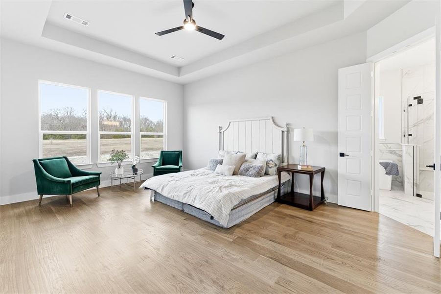 Bedroom featuring a raised ceiling, a ceiling fan, and light wood finished floors