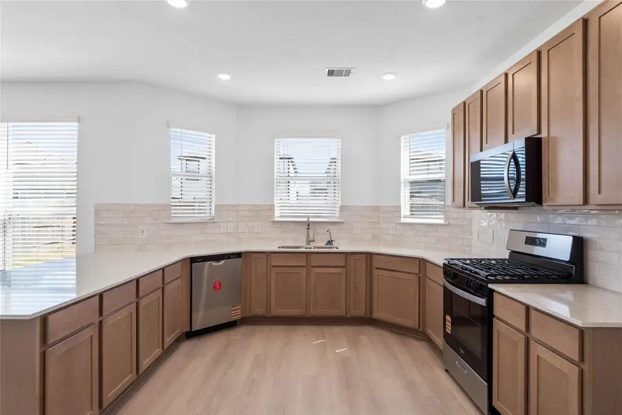 This spacious kitchen boasts high ceilings, recessed lighting, Woodmont Dakota cabinets in a Barley stain, Silestone Lusso countertops, stainless steel Whirlpool appliances, a modern Daltile backsplash, an extended breakfast bar countertop, and a pantry—all overlooking the expansive family room. This spacious kitchen boasts high ceilings, recessed lighting, Woodmont Dakota cabinets in a Barley stain, Silestone Lusso countertops, stainless steel Whirlpool appliances, a modern Daltile backsplash, an extended breakfast bar countertop, and a pantry—all overlooking the expansive family room.
