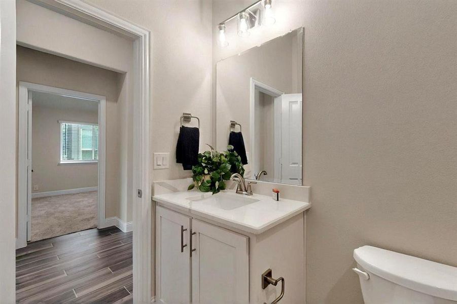 Half bath featuring toilet, wood finished floors, vanity, and baseboards