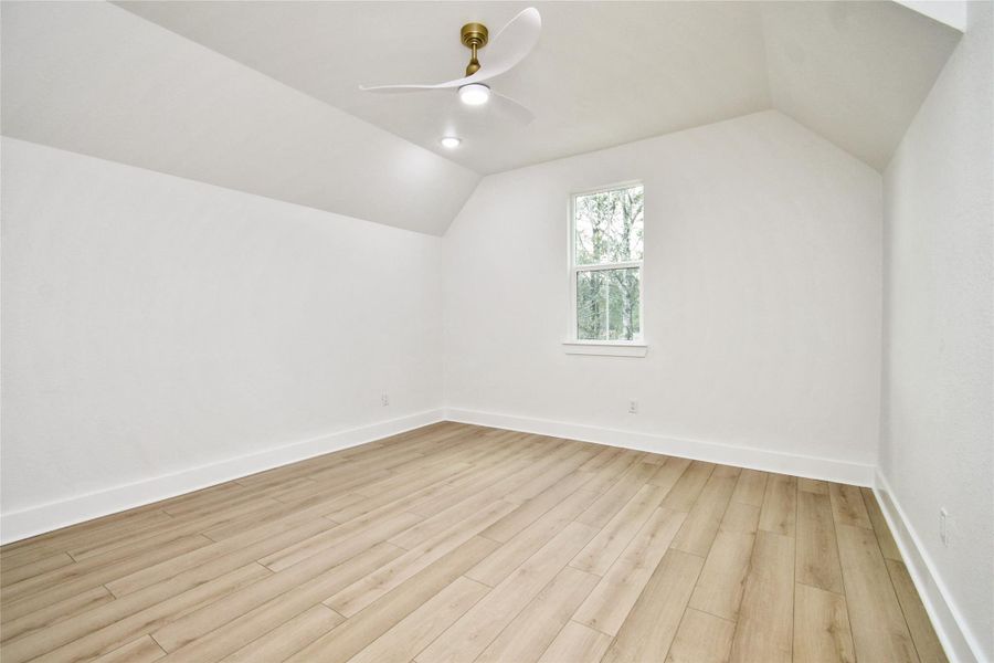 This secondary bedroom offers a peaceful retreat with warm wood-look flooring and a modern aerodynamic ceiling fan. Large windows invite natural light, while the neutral palette creates a calm, restful atmosphere.
