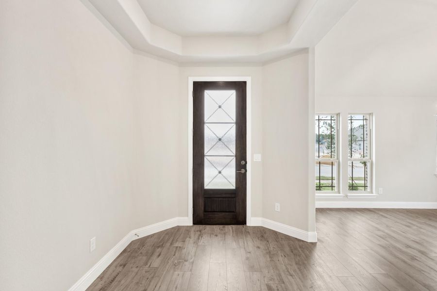 Entryway with dark wood front door with glass panels, tray ceiling, and light hardwood floors