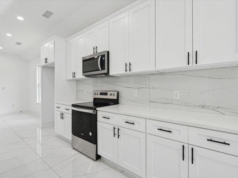 Kitchen featuring light stone countertops, light tile patterned floors, stainless steel appliances, decorative backsplash, and white cabinets