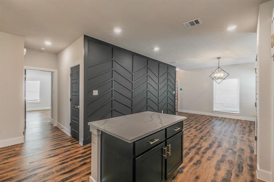 Kitchen with light stone counters, dark wood-type flooring, pendant lighting, an inviting chandelier, and a center island