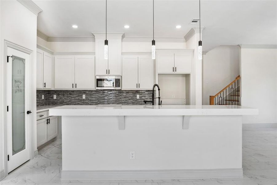 Kitchen featuring crown molding, light finish floors, decorative backsplash, an island with sink, and stainless steel microwave Kitchen featuring crown molding, light finish floors, decorative backsplash, an island with sink, and stainless steel microwave