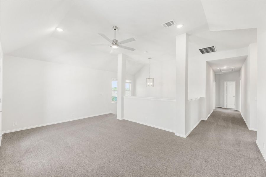 Open living area with vaulted ceiling, ceiling fan, gray carpet, and hallway leading to bedrooms