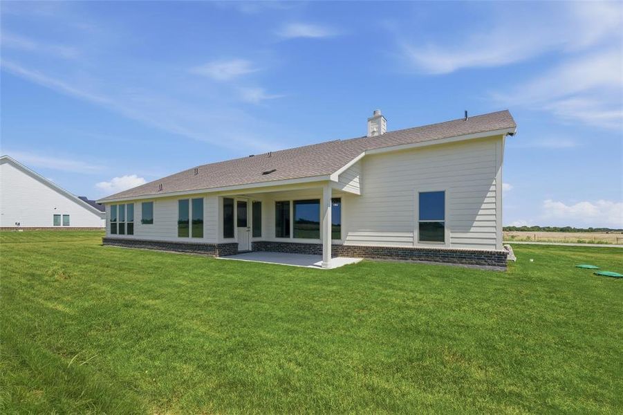 Rear exterior featuring a covered patio, extensive green lawn, white horizontal siding, and a dark stone veneer foundation Rear exterior featuring a covered patio, extensive green lawn, white horizontal siding, and a dark stone veneer foundation