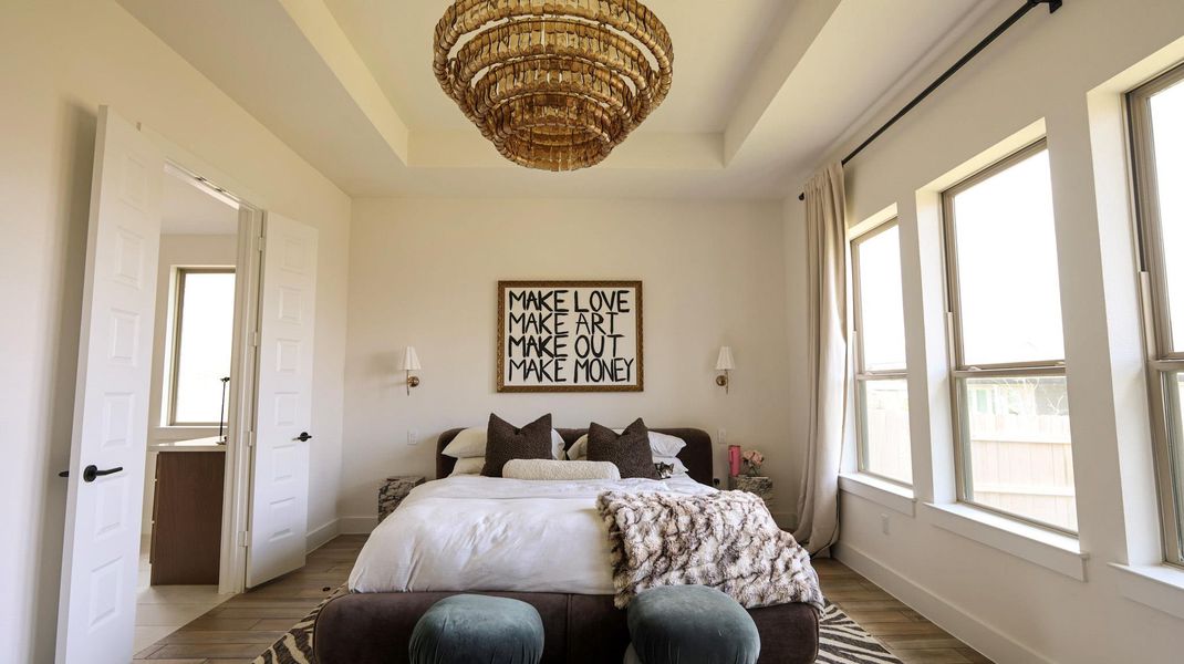 Natural light floods this primary bedroom featuring tray ceilings and rich wood flooring. Natural light floods this primary bedroom featuring tray ceilings and rich wood flooring.