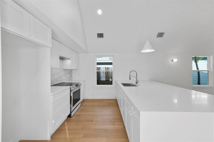 Kitchen with light wood-type flooring, lofted ceiling, sink, white cabinetry, and electric stove