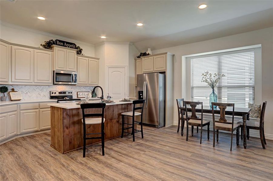 Kitchen featuring stainless steel appliances, a center island with sink, light wood-type flooring, backsplash, and a breakfast bar