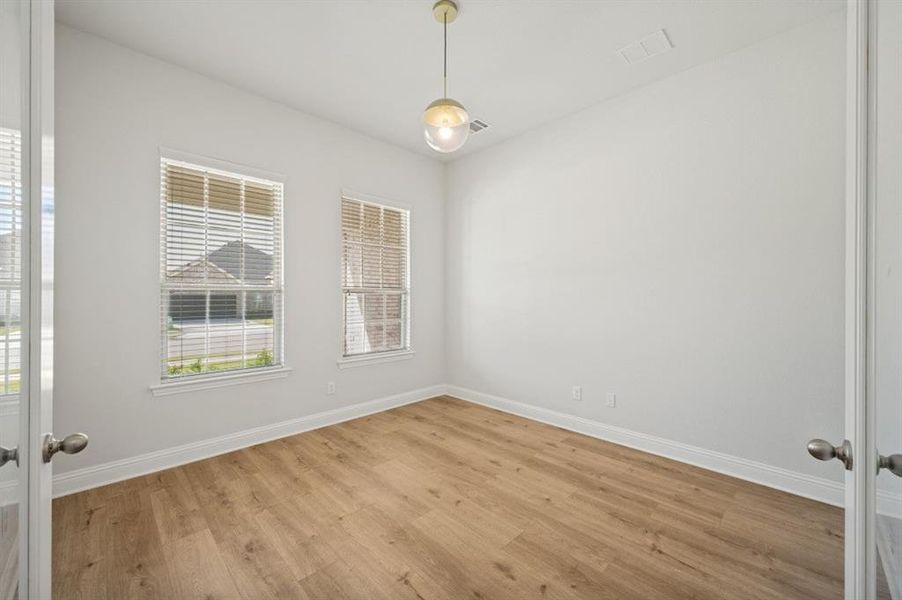 Bright room featuring two windows with horizontal blinds, wood-finish flooring, and a contemporary pendant light fixture