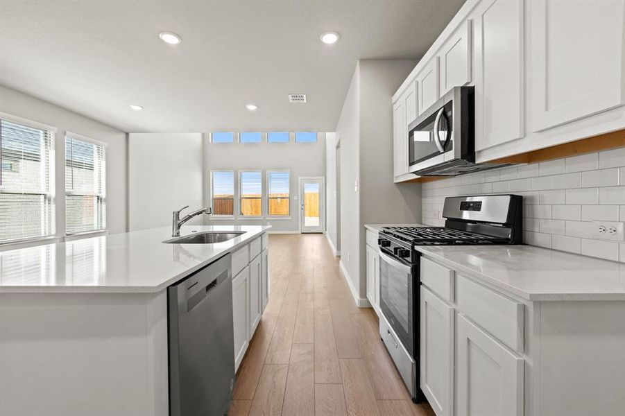 Kitchen featuring white cabinetry, appliances with stainless steel finishes, sink, light wood-type flooring, and a center island with sink