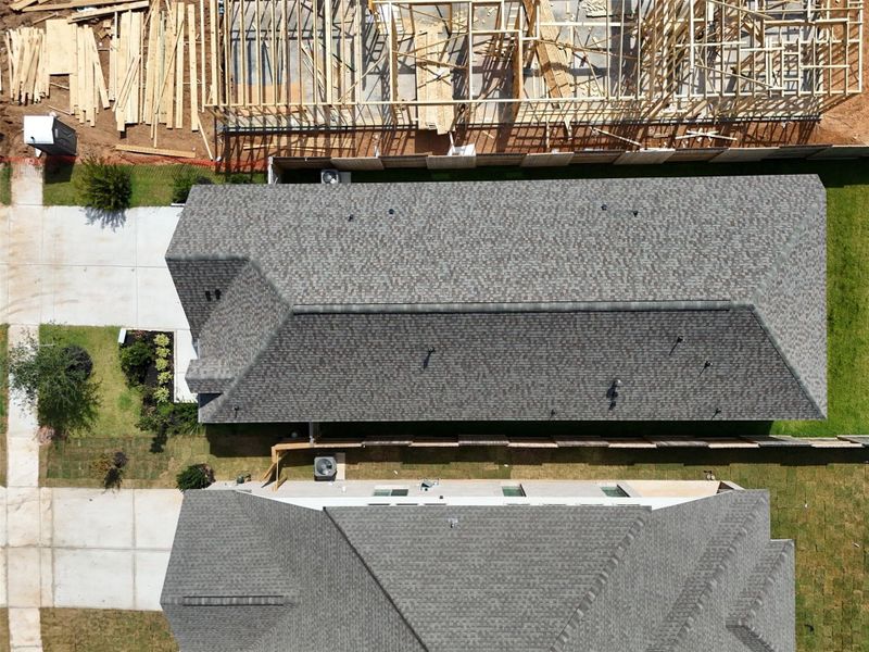 Aerial view of a residential neighborhood showcasing a completed home with a well-maintained roof and adjacent property under construction, highlighting ongoing development and growth in the area.