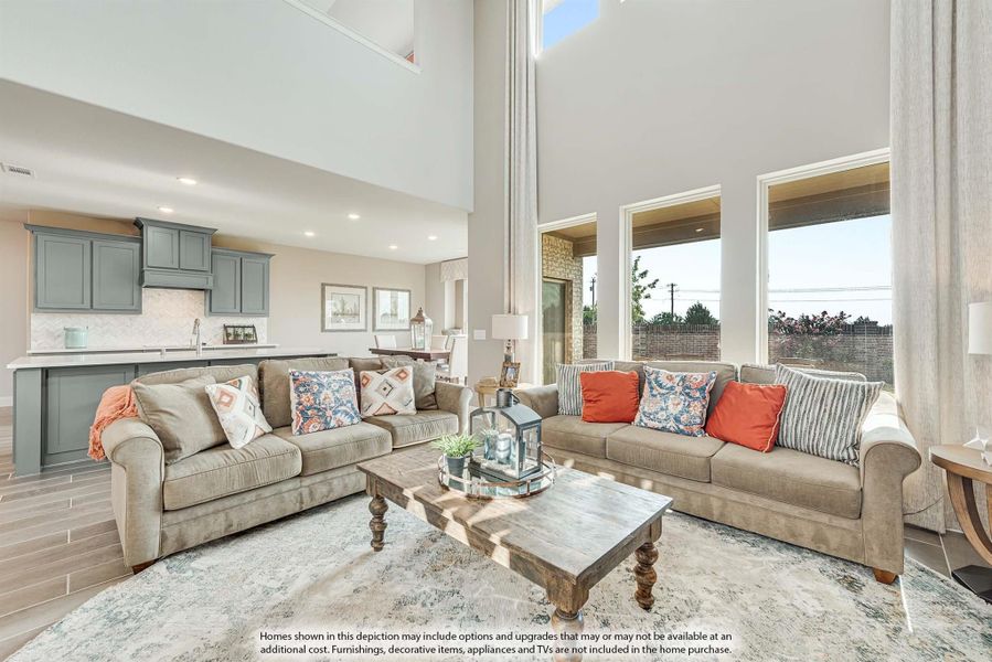 Open-concept living room with two-story ceiling, two sofas, and kitchen with gray cabinets in background