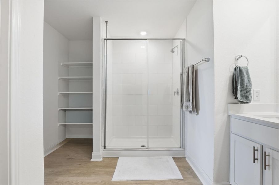 Spacious bathroom featuring a glass-enclosed shower, built-in shelving, wood-finish flooring, a contemporary vanity with a countertop, and modern cabinet hardware