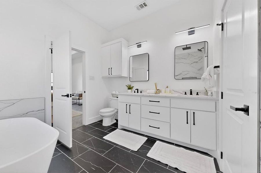 Bathroom with a freestanding bath, double vanity, and dark marble finish flooring