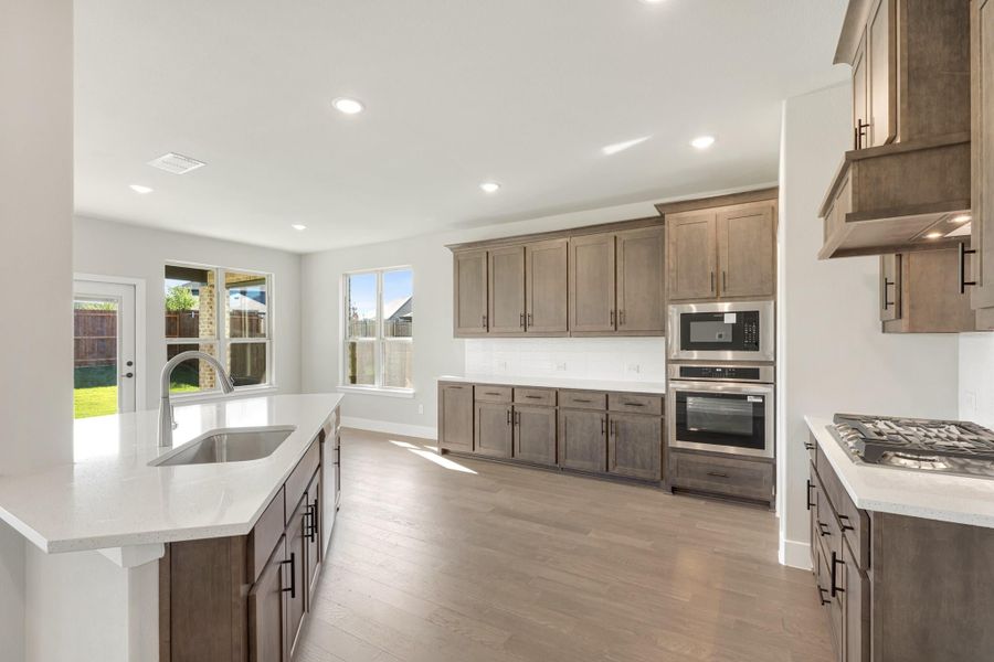 Kitchen with dark brown cabinets, white quartz countertops, stainless steel appliances, and hardwood floors