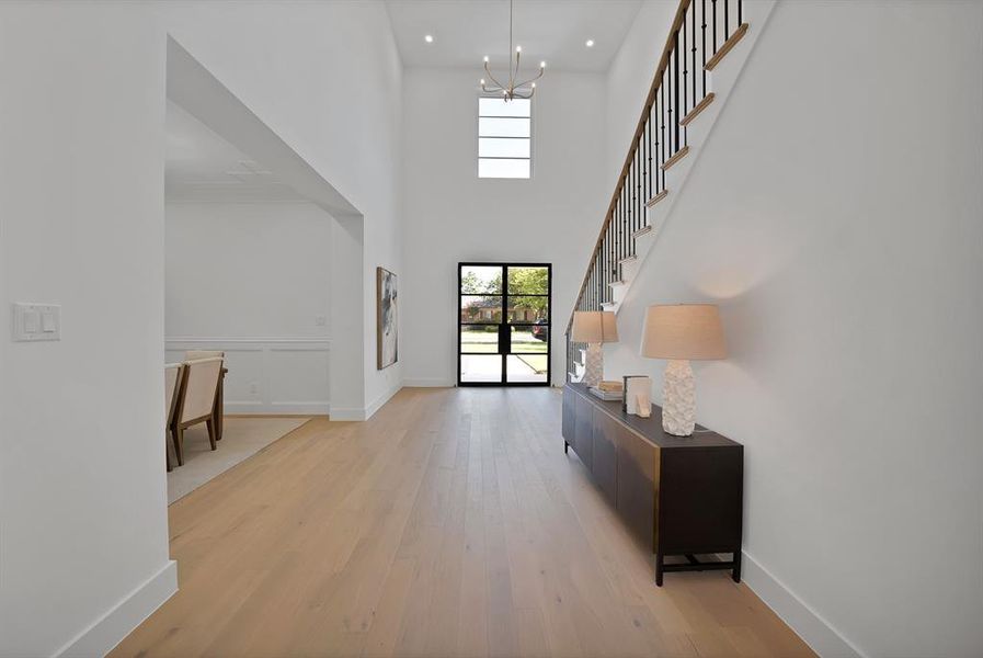 Two-story entryway featuring wood-finish flooring, a contemporary chandelier, a metal-framed glass front door, and a staircase with black iron spindles and wood handrails