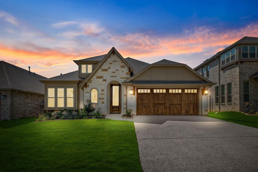 Single-story home with stone exterior, wood garage doors, arched entry, and green lawn at dusk